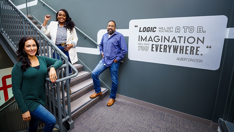Three associates on an interior staircase next to a quote painted on the wall