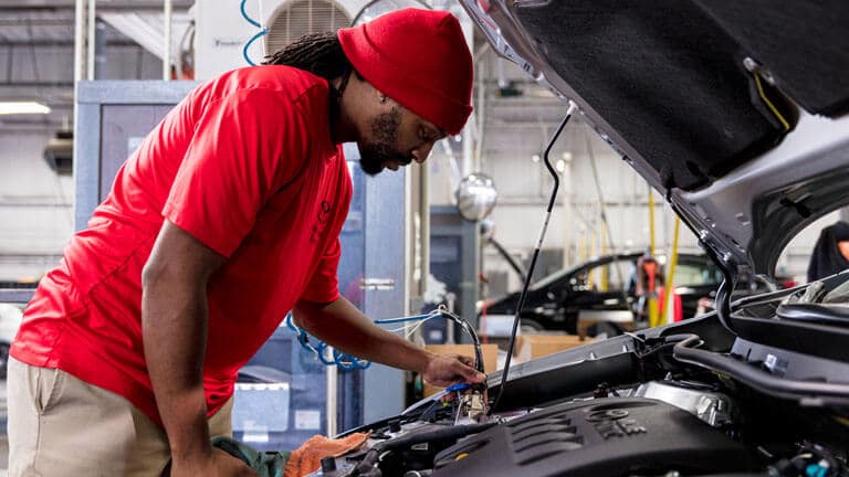 JM Family associate in a red shirt and beanie, working on an engine under an open hood