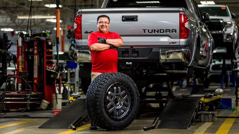 JM Family associate standing beside a Tundra truck on the production floor, smiling, arms crossed